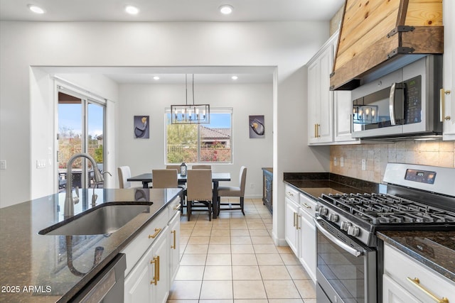 kitchen featuring stainless steel appliances, backsplash, white cabinets, a sink, and dark stone countertops