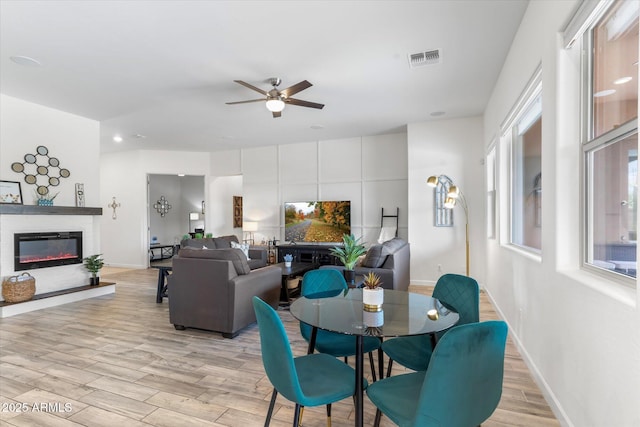 dining area featuring a glass covered fireplace, visible vents, plenty of natural light, and light wood finished floors