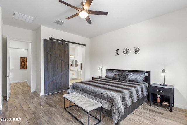 bedroom featuring a barn door, light wood-style flooring, and visible vents