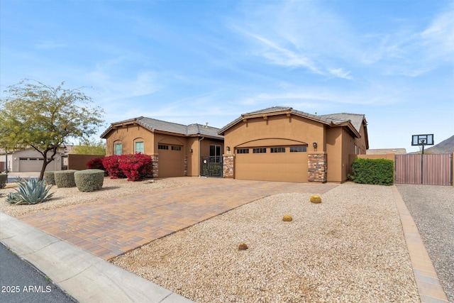 mediterranean / spanish-style home with an attached garage, fence, stone siding, decorative driveway, and stucco siding