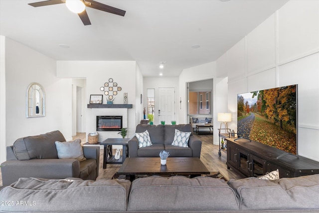 living room with a glass covered fireplace, ceiling fan, and wood finished floors