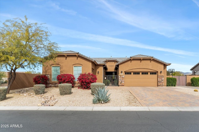 mediterranean / spanish-style house featuring a fenced front yard, decorative driveway, a garage, and stucco siding