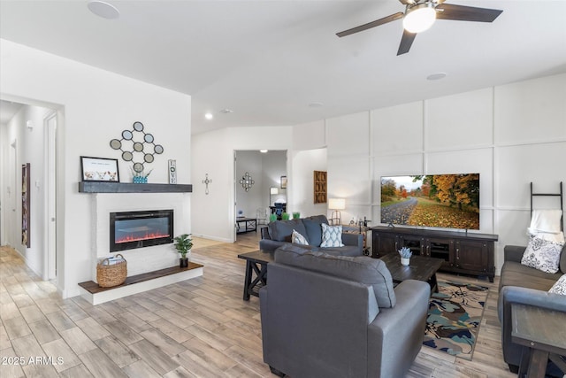 living room featuring light wood-style floors, a glass covered fireplace, and a ceiling fan