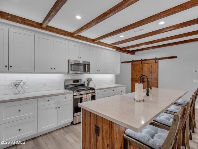 956 S Torrey Pines Dr, Williams, AZ 86046 - kitchen featuring appliances with stainless steel finishes, a barn door, beamed ceiling, light wood-style flooring, and a breakfast bar