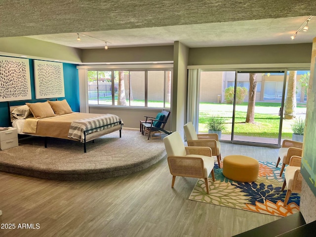 bedroom with rail lighting, access to exterior, wood finished floors, and a textured ceiling