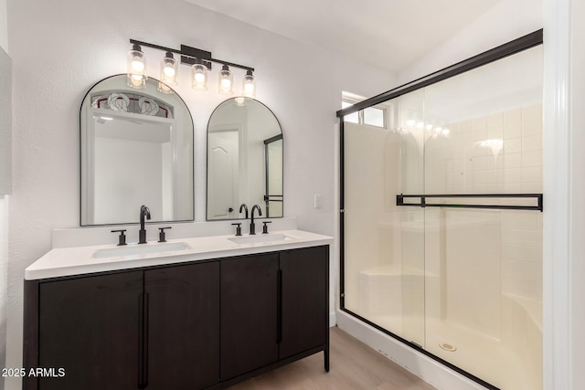 bathroom with double vanity, wood finished floors, a stall shower, and a sink