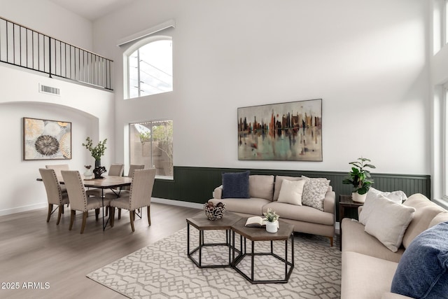 living room featuring a wainscoted wall, a high ceiling, wood finished floors, and visible vents