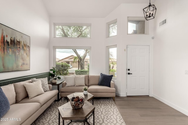 living room with visible vents, baseboards, a chandelier, a high ceiling, and wood finished floors