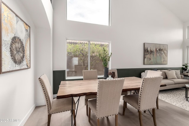 dining space with wood finished floors, a towering ceiling, and wainscoting