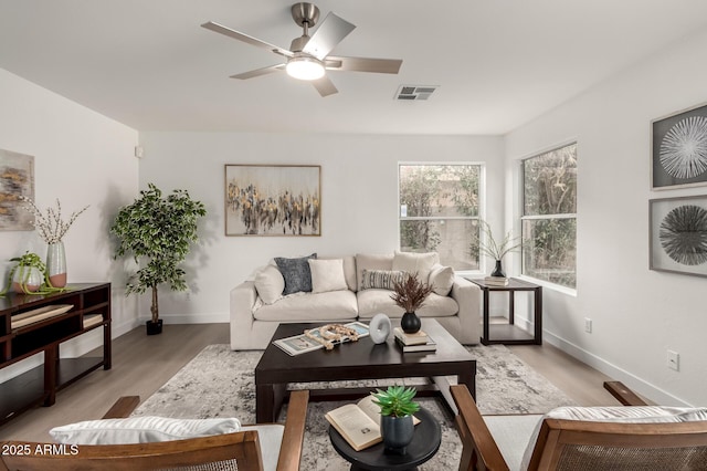 living area with visible vents, baseboards, light wood-style floors, and a ceiling fan