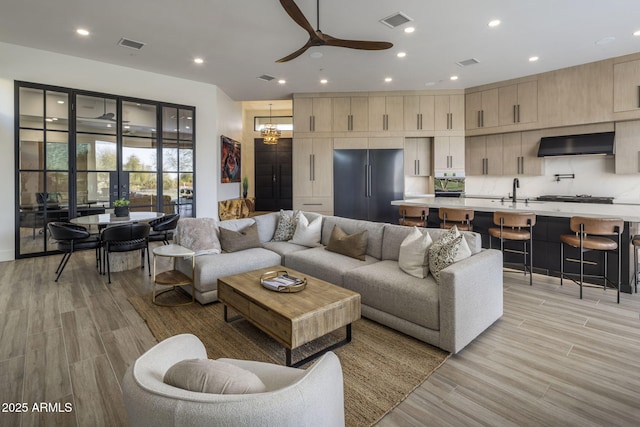 living room featuring sink, ceiling fan with notable chandelier, and light hardwood / wood-style floors