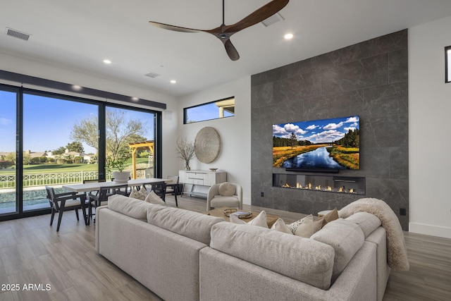 living room with a tiled fireplace, wood-type flooring, and ceiling fan