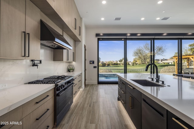 kitchen featuring tasteful backsplash, sink, dishwashing machine, black gas stove, and wall chimney range hood