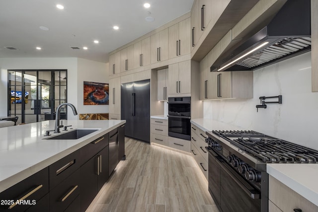 kitchen with sink, backsplash, black appliances, wall chimney range hood, and light wood-type flooring