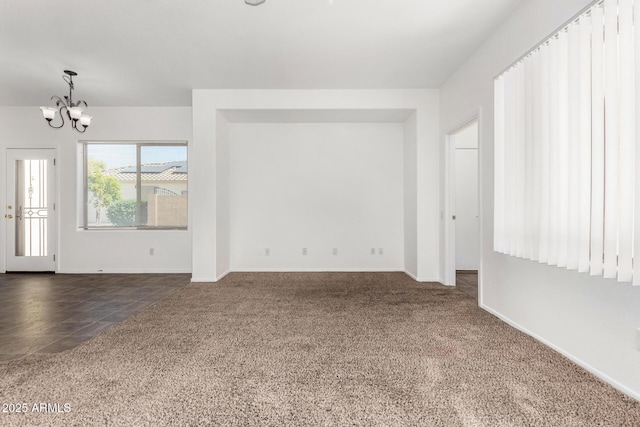 spare room featuring dark colored carpet and an inviting chandelier