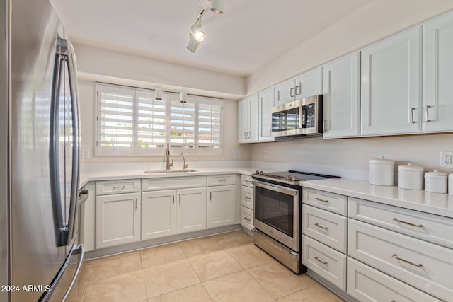 kitchen with appliances with stainless steel finishes, sink, track lighting, white cabinetry, and light tile patterned floors