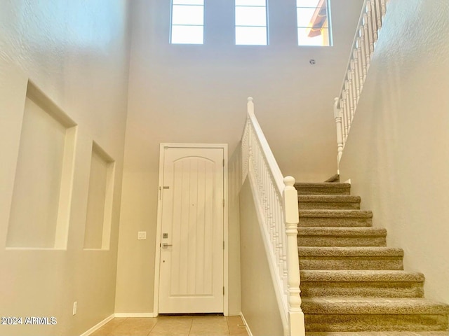 stairway with a high ceiling, plenty of natural light, and tile patterned flooring