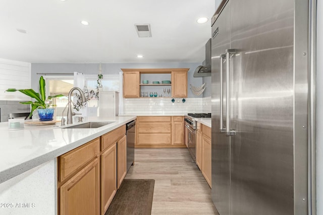 kitchen featuring sink, wall chimney exhaust hood, backsplash, light stone counters, and high end appliances