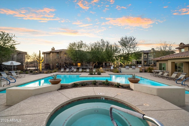 pool at dusk featuring a patio and a hot tub