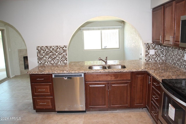 kitchen featuring light stone counters, sink, kitchen peninsula, stainless steel appliances, and backsplash