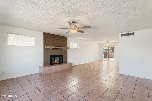 unfurnished living room featuring a brick fireplace, light tile patterned floors, a textured ceiling, and ceiling fan