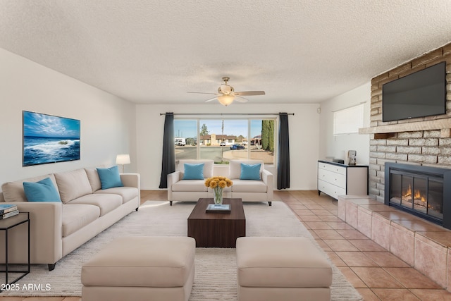 tiled living room featuring ceiling fan, a textured ceiling, and a fireplace