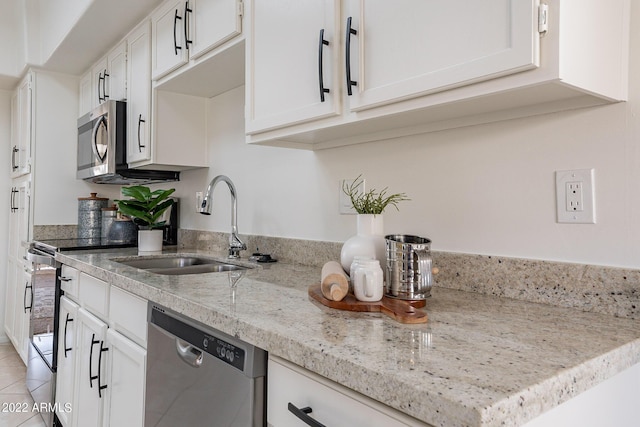 kitchen featuring light tile patterned floors, light stone countertops, a sink, appliances with stainless steel finishes, and white cabinetry