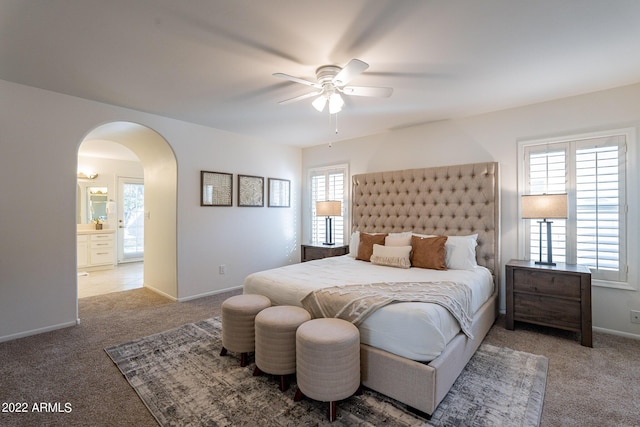 carpeted bedroom featuring baseboards, arched walkways, and a ceiling fan