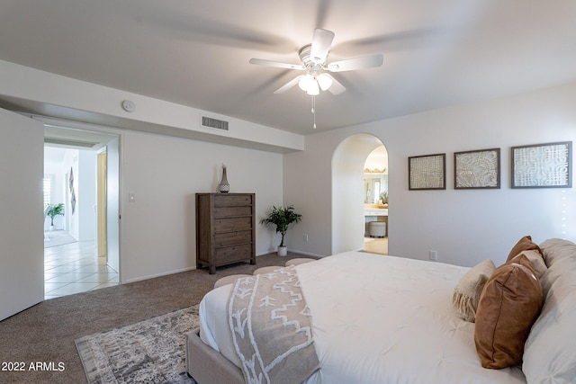 tiled bedroom featuring visible vents, ceiling fan, carpet floors, arched walkways, and ensuite bath