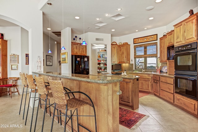 kitchen featuring stone counters, hanging light fixtures, kitchen peninsula, decorative backsplash, and black appliances