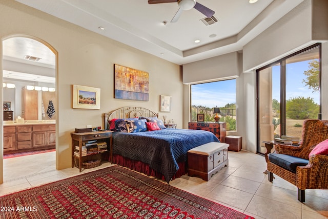 tiled bedroom featuring a raised ceiling, ceiling fan, and ensuite bathroom