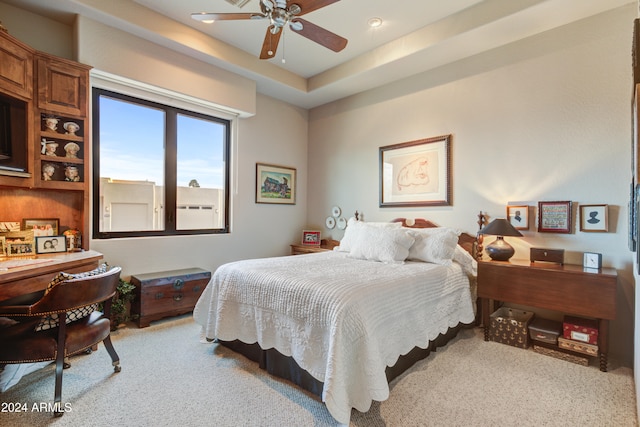 bedroom featuring light colored carpet, a raised ceiling, and ceiling fan