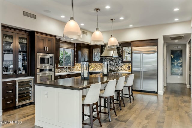 6929 E Montreal Pl, Scottsdale, AZ 85254 - kitchen featuring built in appliances, wall chimney range hood, dark countertops, visible vents, and beverage cooler
