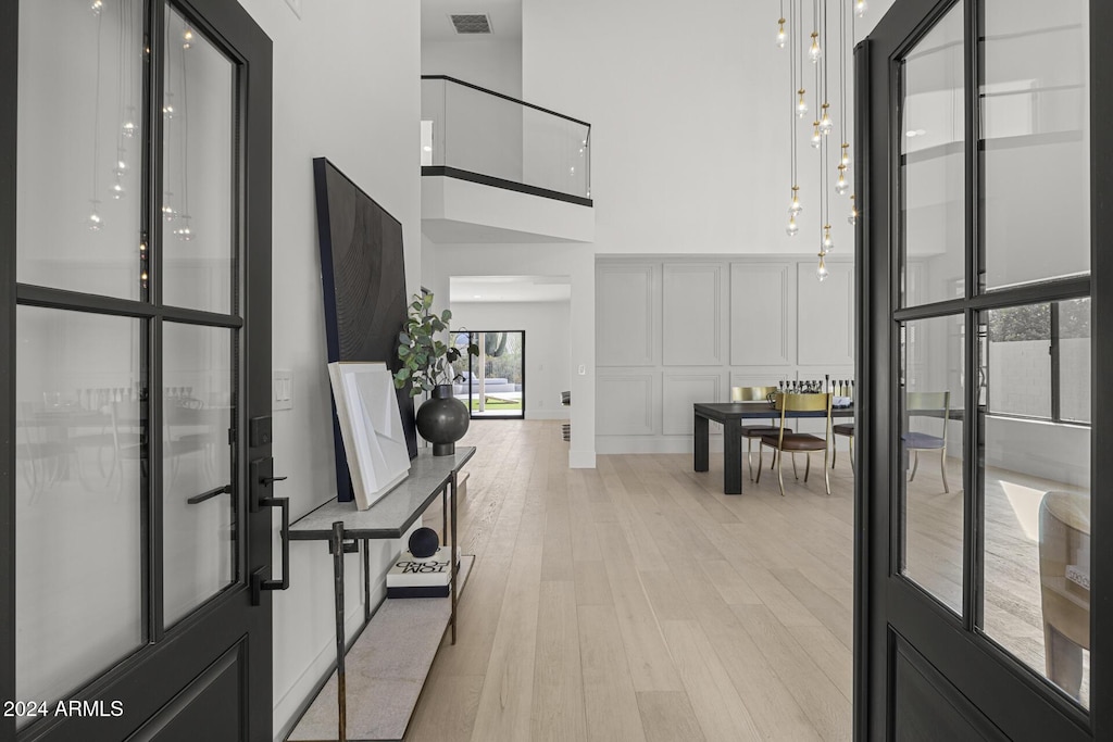 hallway with a high ceiling, light hardwood / wood-style floors, and french doors