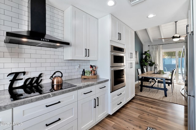 kitchen featuring tasteful backsplash, lofted ceiling with beams, appliances with stainless steel finishes, wood finished floors, and wall chimney exhaust hood