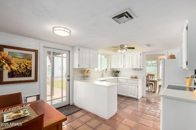 kitchen with visible vents, a sink, light countertops, white cabinets, and backsplash