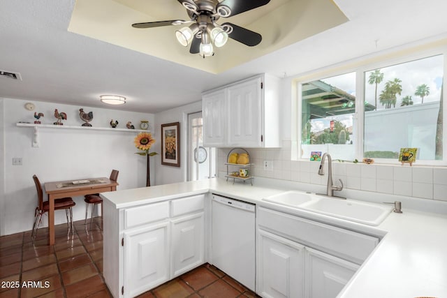 kitchen featuring visible vents, decorative backsplash, a peninsula, white dishwasher, and a sink