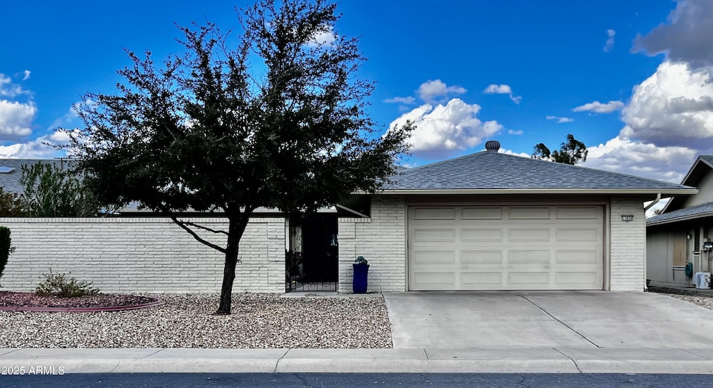 single story home featuring a shingled roof, concrete driveway, brick siding, and an attached garage