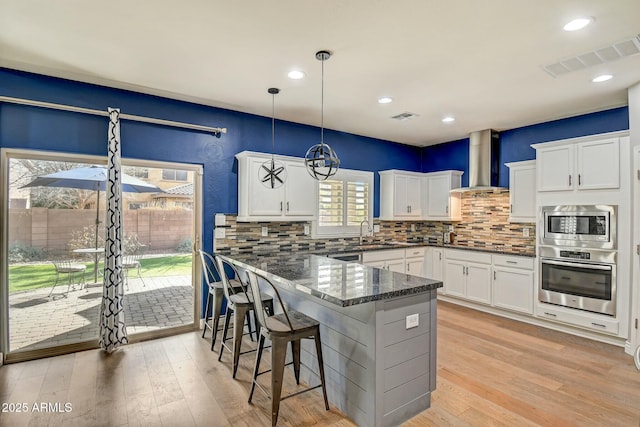 10249 E Kinetic Dr, Mesa, AZ 85212 - kitchen featuring stainless steel appliances, wall chimney range hood, white cabinets, backsplash, and a kitchen bar