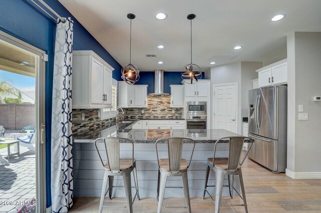10249 E Kinetic Dr, Mesa, AZ 85212 - kitchen featuring appliances with stainless steel finishes, wall chimney exhaust hood, a peninsula, backsplash, and dark stone countertops