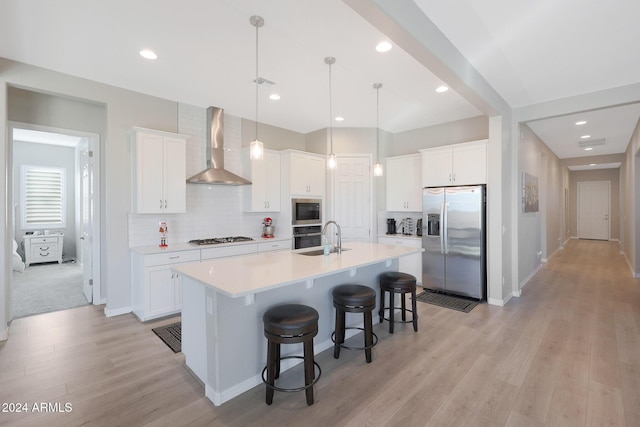 kitchen with a kitchen breakfast bar, a sink, stainless steel appliances, wall chimney exhaust hood, and an island with sink