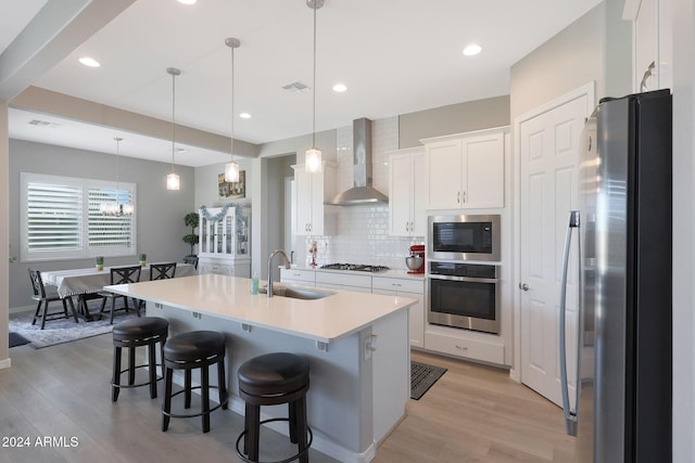 kitchen featuring light wood-type flooring, a sink, wall chimney exhaust hood, and stainless steel appliances