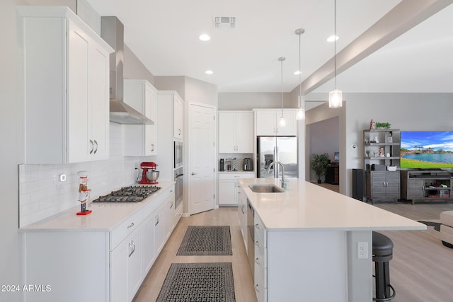 kitchen with visible vents, wall chimney range hood, light wood-type flooring, a sink, and stainless steel appliances