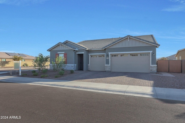 view of front of home with board and batten siding, driveway, fence, an attached garage, and stone siding