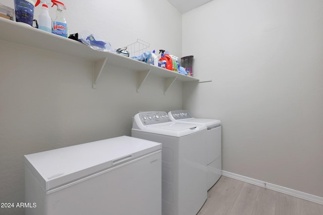 clothes washing area featuring washing machine and clothes dryer, laundry area, baseboards, and light wood-style flooring