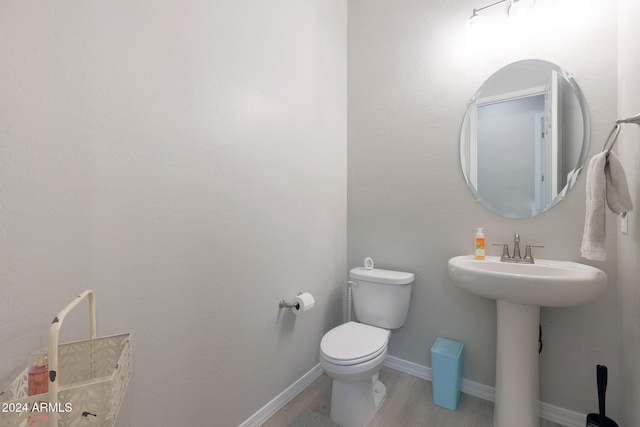 half bath with baseboards, a sink, wood finished floors, and toilet