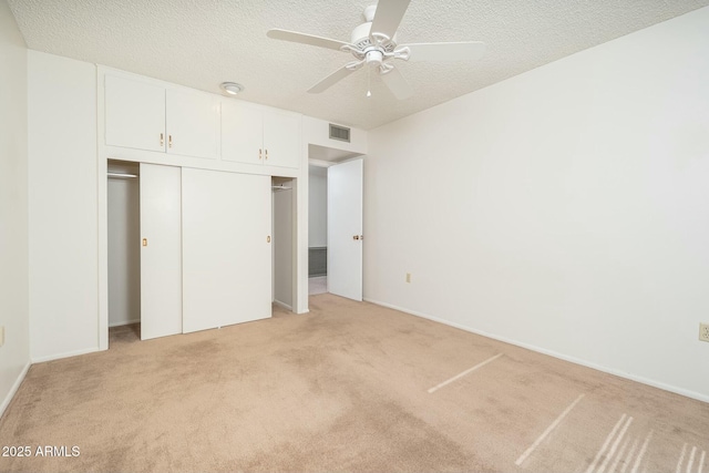 unfurnished bedroom featuring light carpet, a textured ceiling, a closet, and ceiling fan