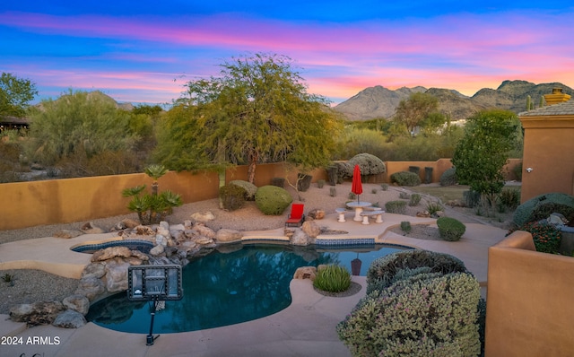 pool at dusk with a mountain view, an in ground hot tub, and a patio area