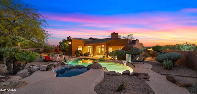 pool at dusk featuring an in ground hot tub and a patio