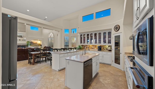 kitchen featuring a center island with sink, white cabinets, stainless steel appliances, and a high ceiling